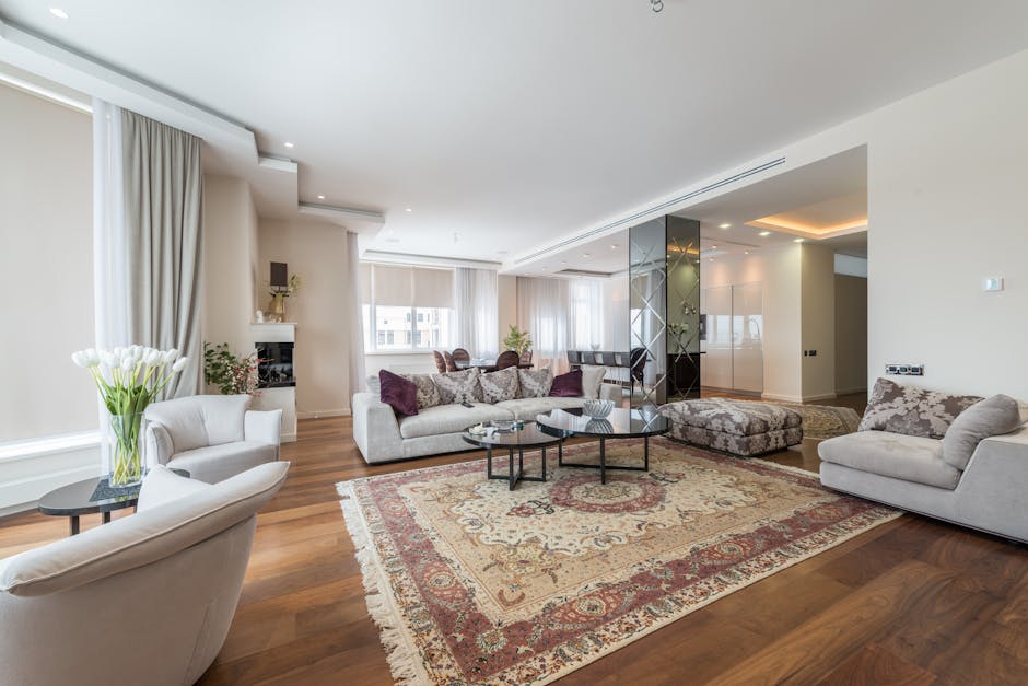 A spacious living room with large, white-framed double-hung windows fitted with horizontal blinds, allowing natural light to illuminate the room. The walls are painted in soft, pastel blue and warm be