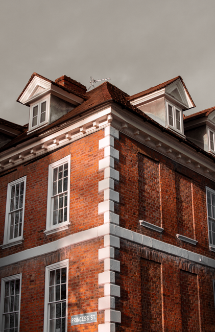 Close-up view of a brick residential building with multiple white-framed double-glazed windows, some with sheer curtains, set into rounded bay window alcoves. The brickwork features a traditional red